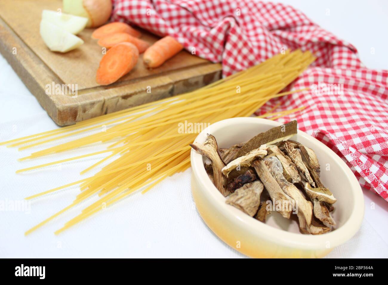 Prodotti alimentari disposti sul tavolo con volant, con quadrati rossi e bianchi. Cucina mediterranea italiana con spaghetti ai funghi porcini secchi. Foto Stock