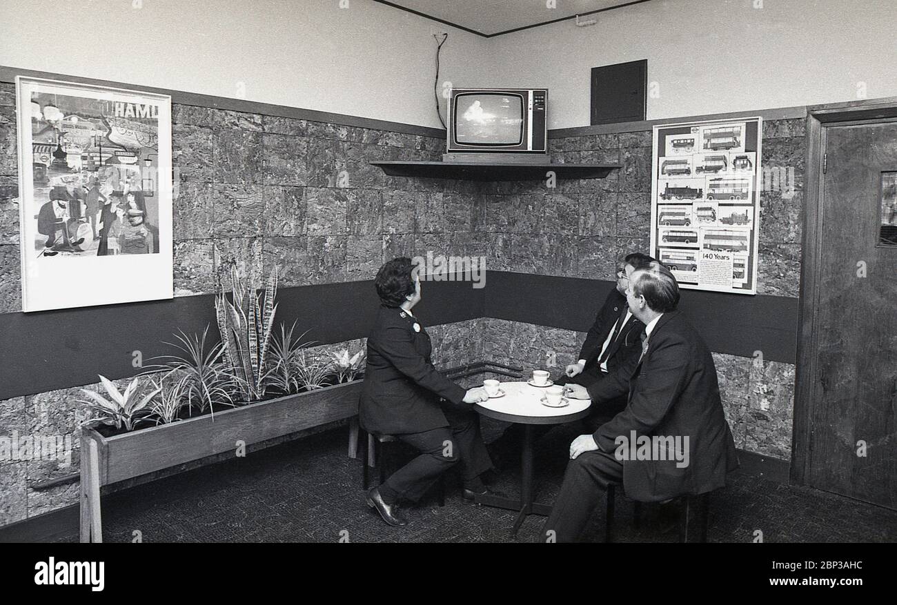 Interno, stanza di riposo del personale dell'autobus New Cross, Londra del sud, Inghilterra, 1974, l'immagine mostra tre membri dell'equipaggio in uniforme che hanno una pausa e una tazza di tè e che guardano una televisione portatile smal. Foto Stock