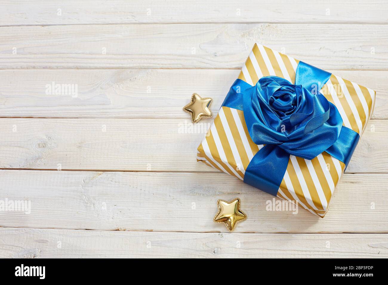 Confezione regalo con archi blu classici. Involucro a righe, stelle dorate su sfondo in legno. Piatto. Vista dall'alto. Foto Stock