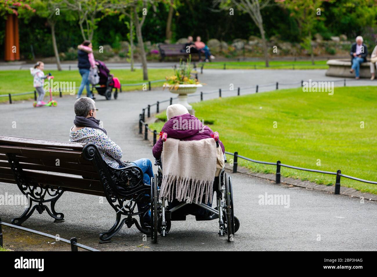 Anziani in sedia a rotelle con tutore seduto accanto a una panchina nel Parco Verde di Santo Stefano`s a Dublino durante il Covid-19 Pandemic Irlanda. Foto Stock