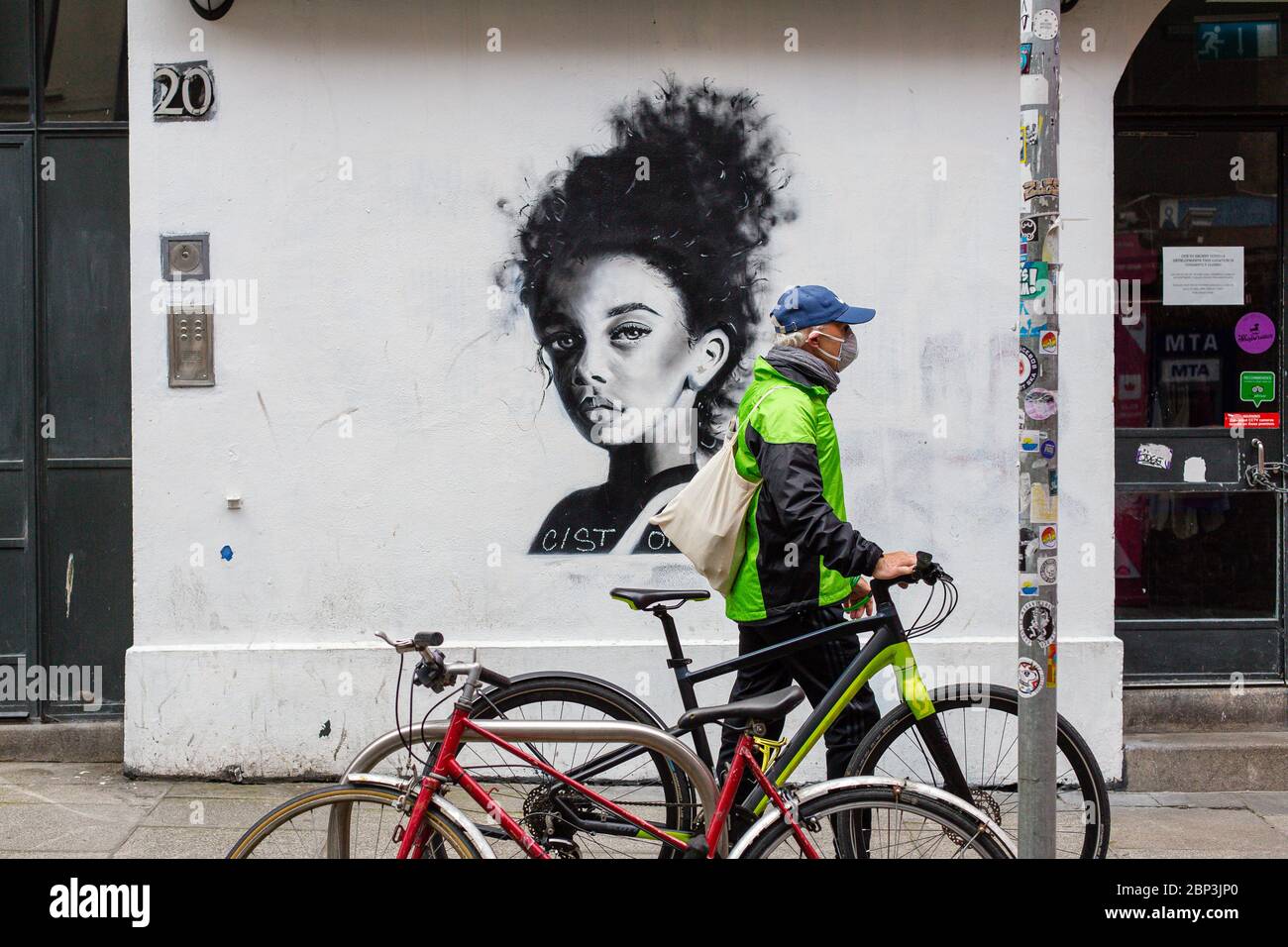 Dublino, Irlanda. Maggio 2020. Uomo con una bicicletta che indossa una maschera protettiva che passa da un murale di una giovane ragazza al Temple Bar, nel centro di Dublino. Foto Stock