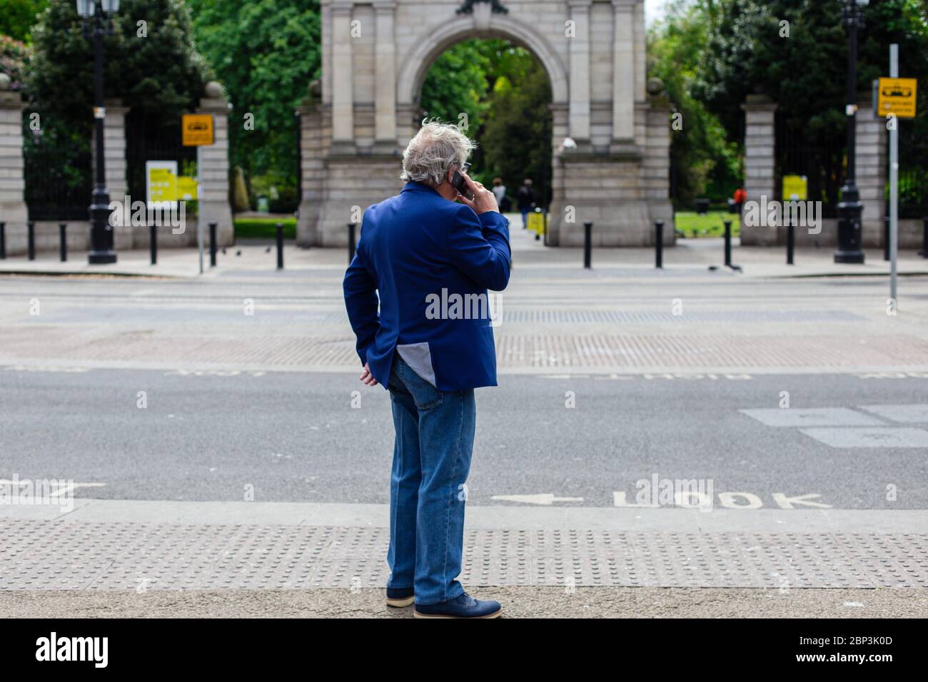 Uomo in tuta che parla al telefono di fronte all'Arco dei Fusiliers - ingresso principale del Parco Verde di Santo Stefano`s a Dublino, Irlanda. Blocco Covid-19. Foto Stock