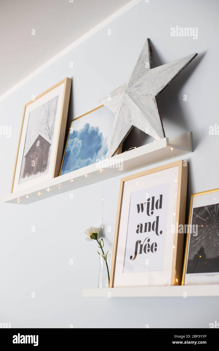 Mensole a muro con una composizione di stampe, una stella di legno e luci a corda. Foto Stock