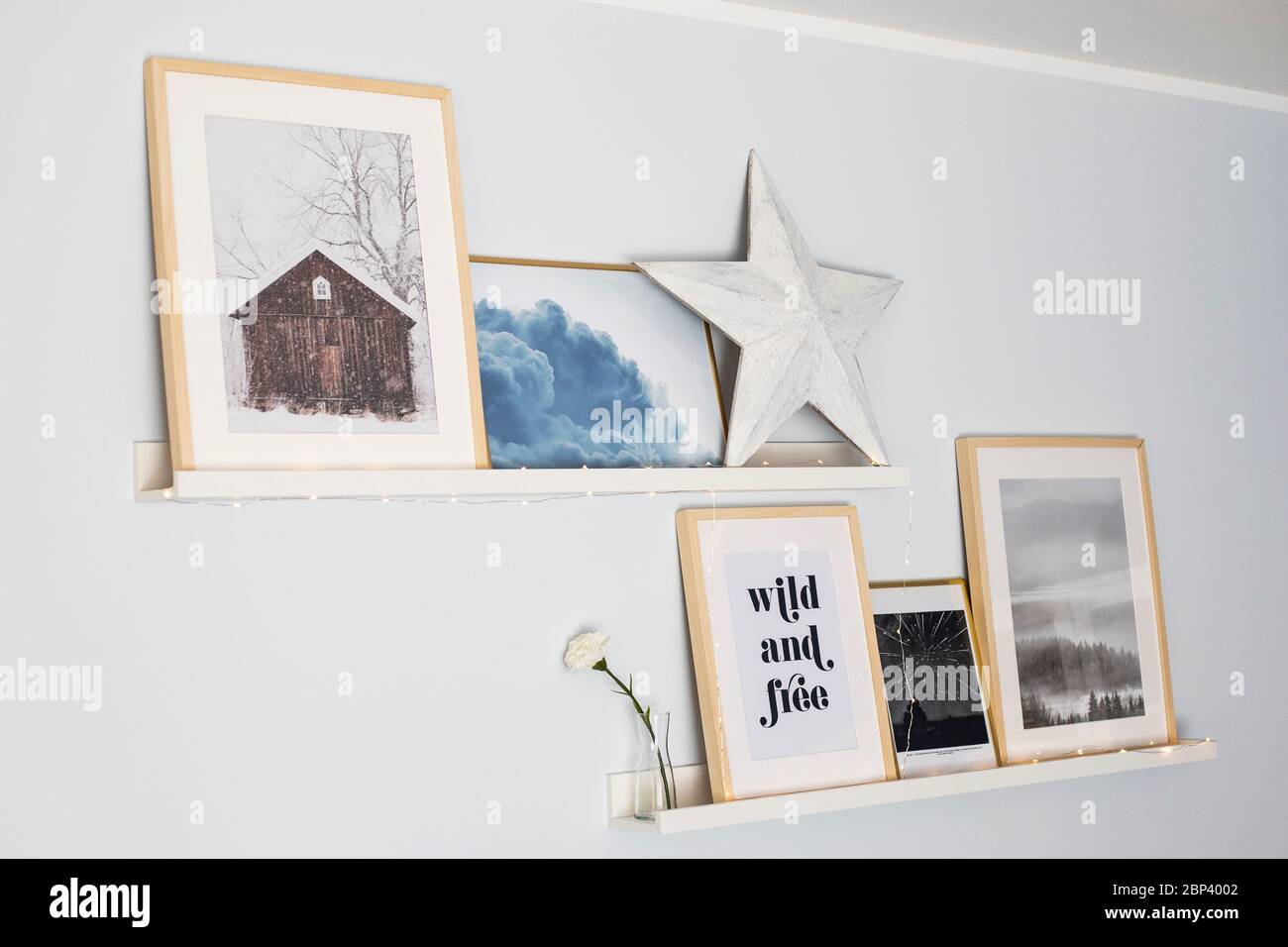 Mensole a muro con una composizione di stampe, una stella di legno e luci a corda. Idea di arredamento. Foto Stock