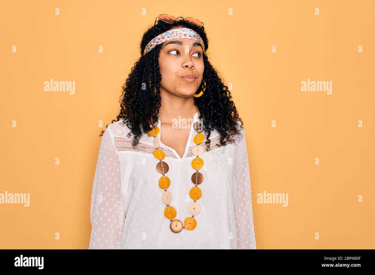 Giovane donna hippie riccia afroamericana che indossa occhiali da sole e  accessori vintage sorridendo guardando al lato e fissando via pensare Foto  stock - Alamy