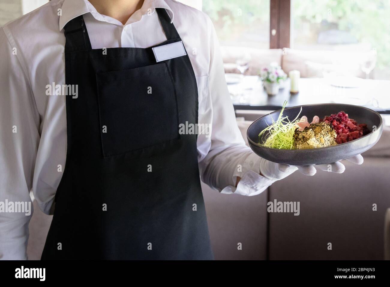 Cameriere che tiene un piatto di catrame di manzo con mirtilli rossi secchi e daikon in un ristorante Foto Stock