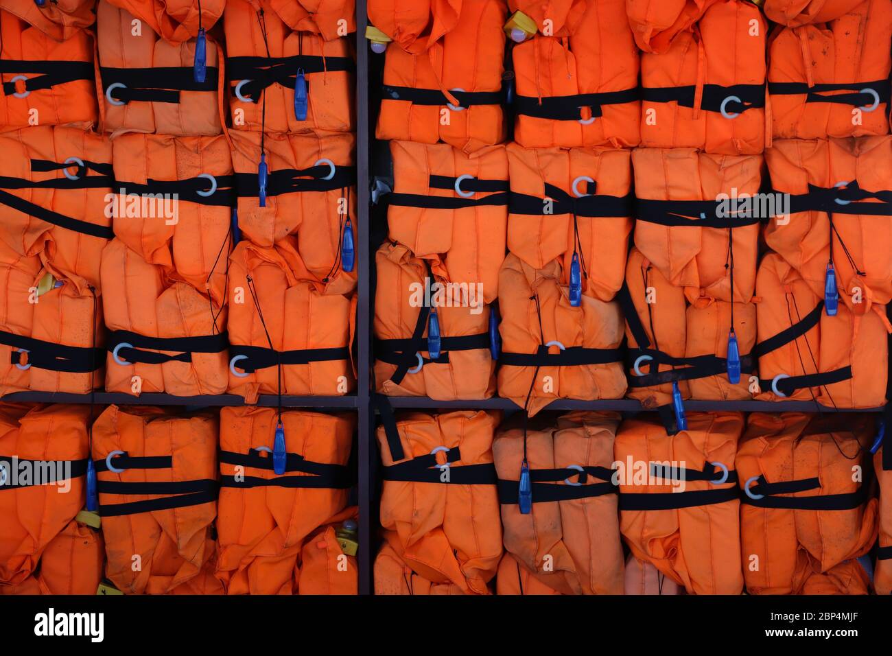 File di giubbotti di salvataggio arancione con cinghie nere e fischi blu accatastati contro un muro su una barca turistica sul canale di Panama. Sfondo Foto Stock
