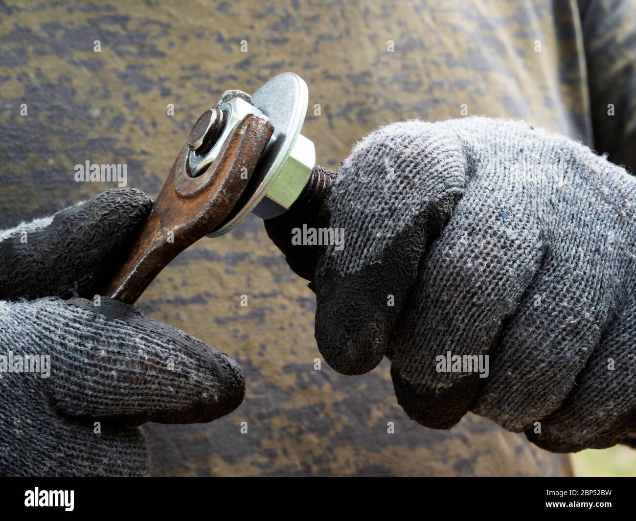 Guanti con mani maschili serrare il dado sul bullone con una chiave Foto Stock