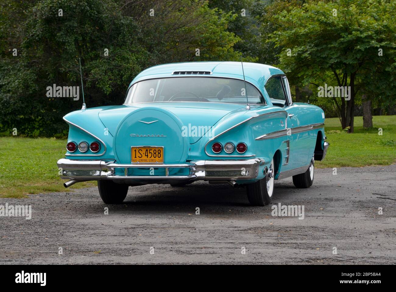 Turquoise 1958 Chevrolet Impala coupé con ruota di scorta posteriore contro alberi vista posteriore tre quarti Foto Stock