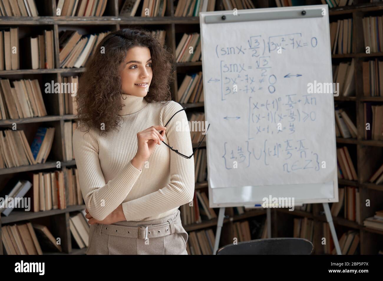 Sorridente giovane insegnante di matematica ispanica che guarda via sognando in classe. Foto Stock