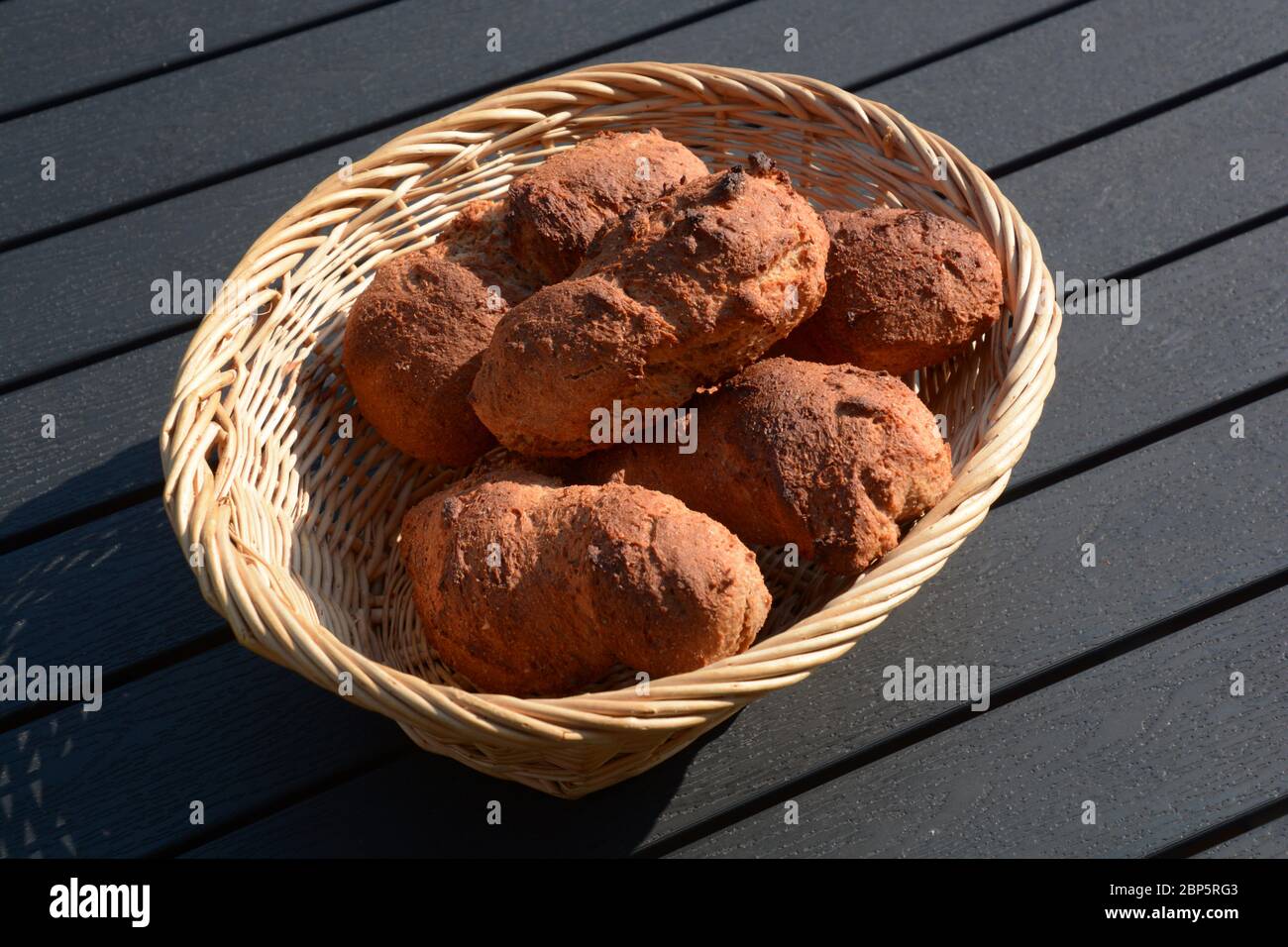 rotoli di grano oblungo freschi fatti in casa in cesto di legno su tavola nera Foto Stock