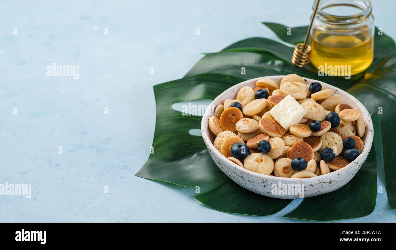 Cibo alla moda - cereali pancake. Un mucchio di mini frittelle di cereali in boul su sfondo blu. Copia spazio a sinistra per il testo. Banner Foto Stock
