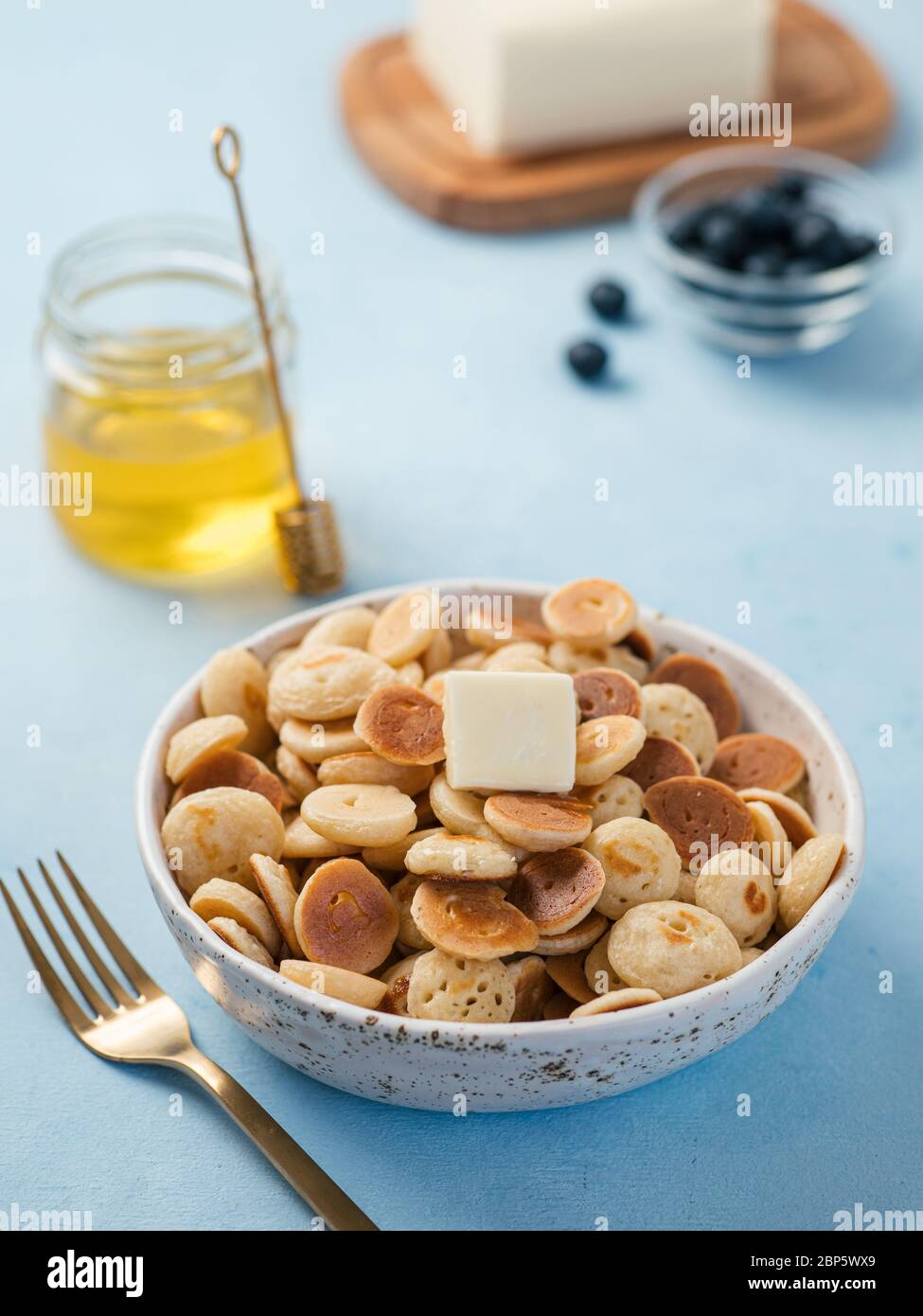 Cibo alla moda - cereali pancake. Un mucchio di mini frittelle di cereali in boul su sfondo blu. Spazio di copia per testo o disegno. Verticale. Foto Stock