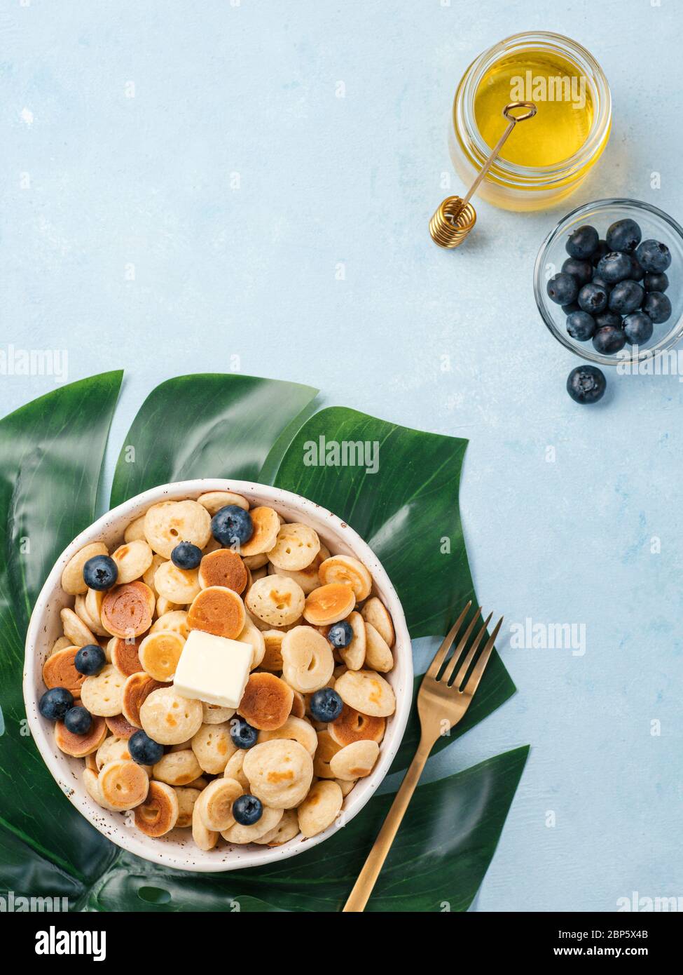 Cibo alla moda - cereali pancake. Un mucchio di mini frittelle di cereali in boul su sfondo blu. Copia spazio a sinistra per il testo. Vista dall'alto o in piano. Verticale. Foto Stock