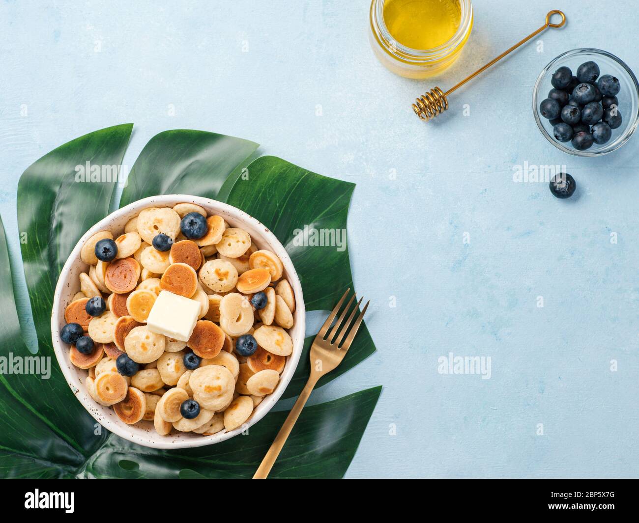 Cibo alla moda - cereali pancake. Un mucchio di mini frittelle di cereali in boul su sfondo blu. Copia spazio a sinistra per il testo. Vista dall'alto o in piano. Foto Stock