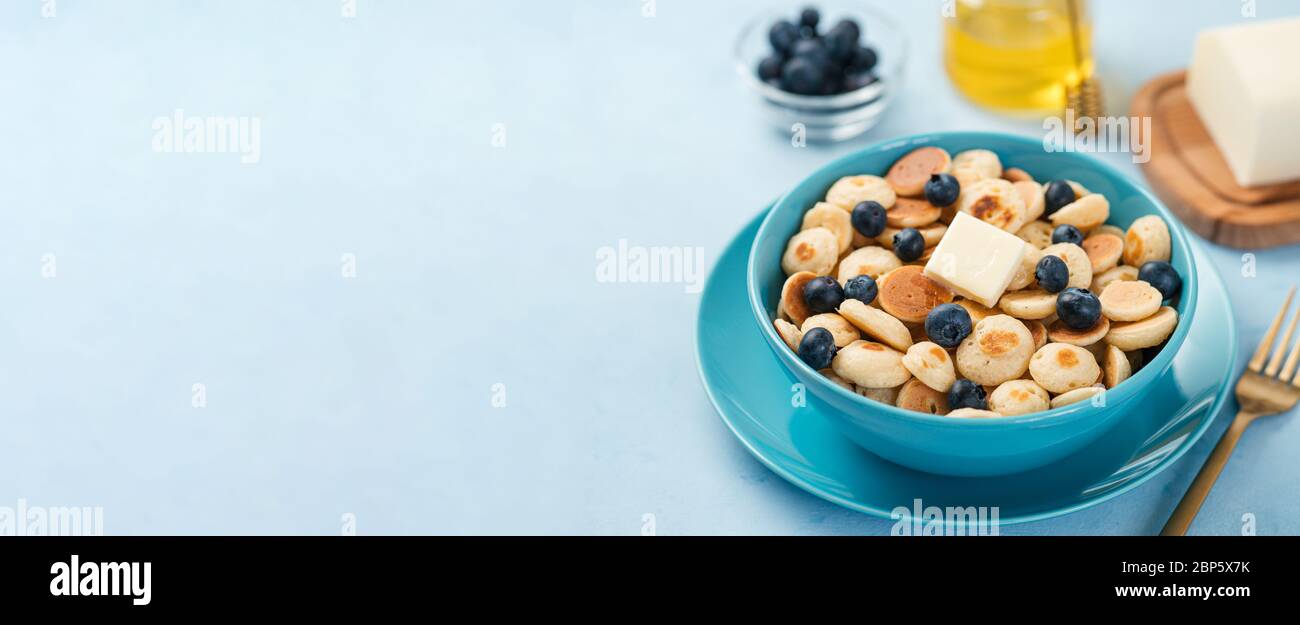 Cibo alla moda - cereali pancake. Un mucchio di mini frittelle di cereali in boul su sfondo blu. Spazio di copia per testo o disegno. Banner orizzontale lungo Foto Stock