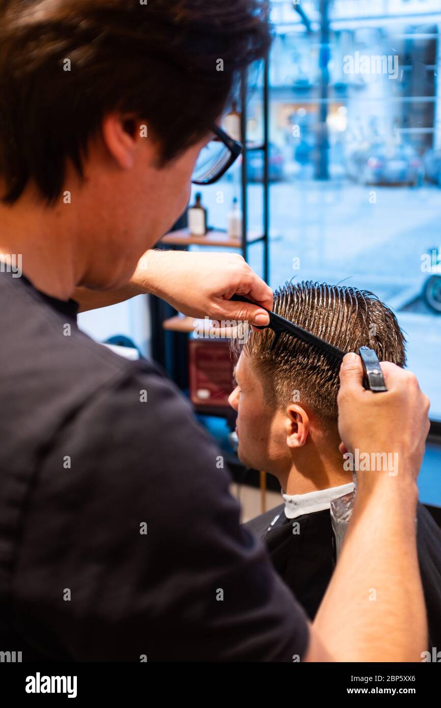 Barber inumidisce i capelli di un giovane con una bottiglia spray nel suo barbiere, pronto per un taglio di capelli Foto Stock