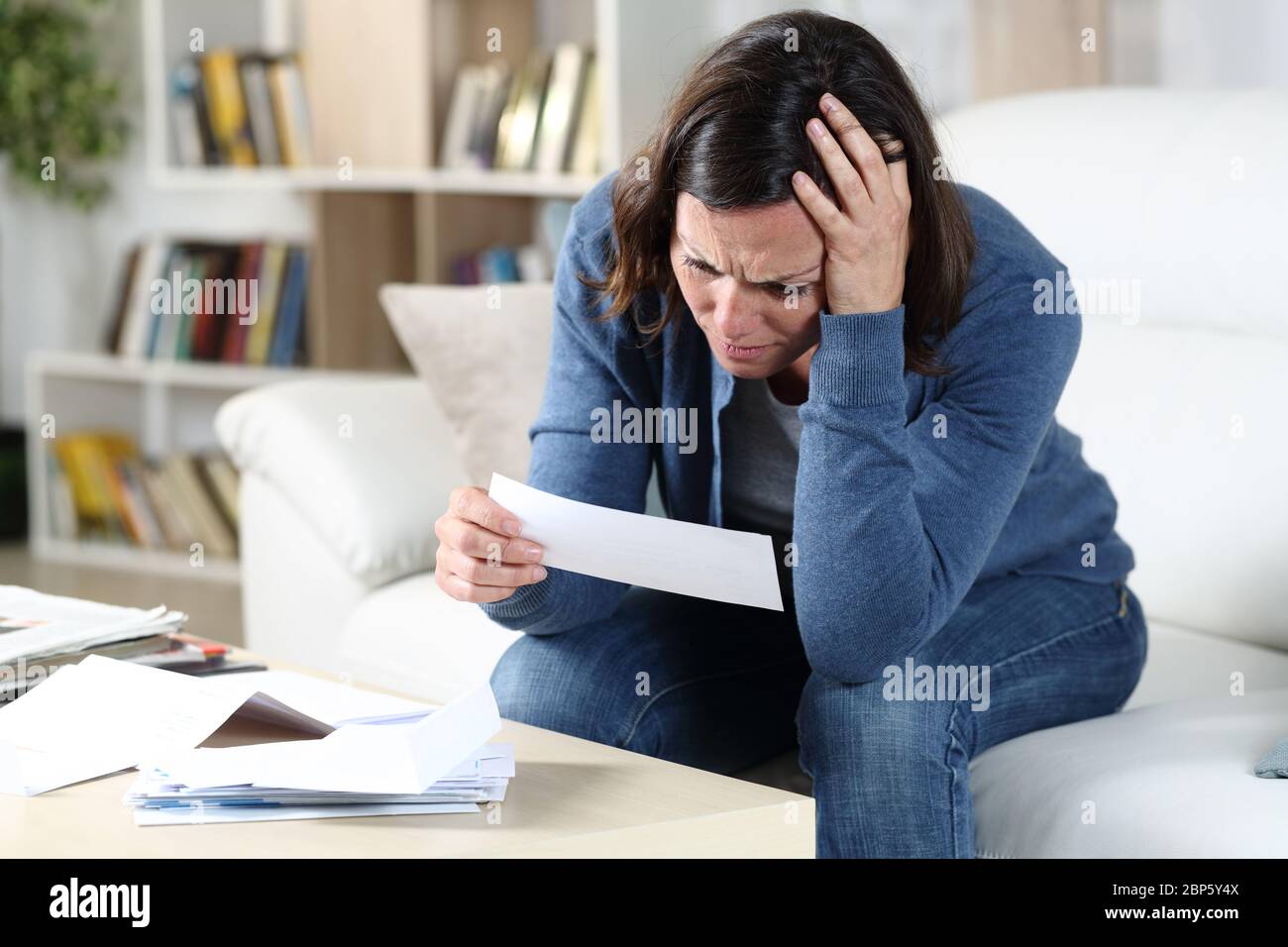 Triste donna adulta che controlla le ricevute seduto nel divano nel soggiorno di casa Foto Stock