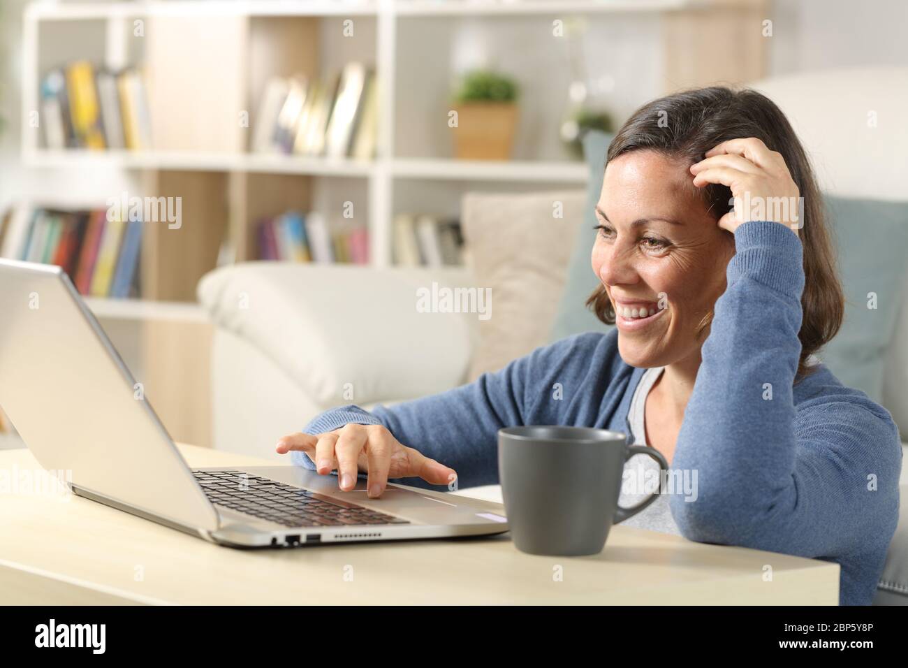 Donna adulta felice che guarda i video online su un computer portatile seduto a casa sul pavimento Foto Stock