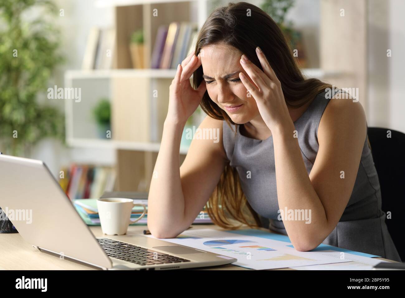 Donna imprenditore che soffre attacco di emicrania seduta su una scrivania a casa Foto Stock
