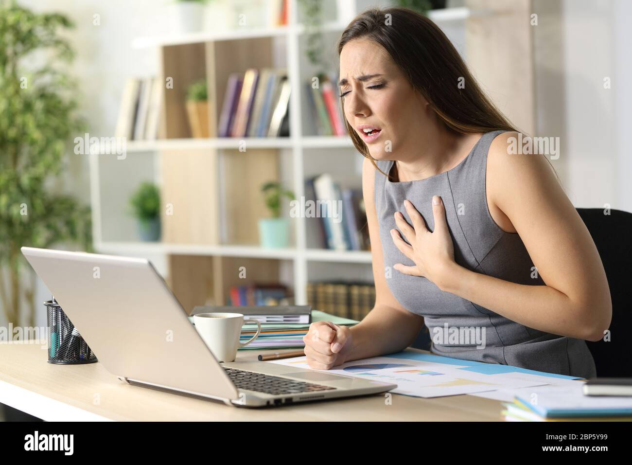 Donna imprenditore sibilante avendo difficoltà di respirazione seduta su una scrivania a casa Foto Stock