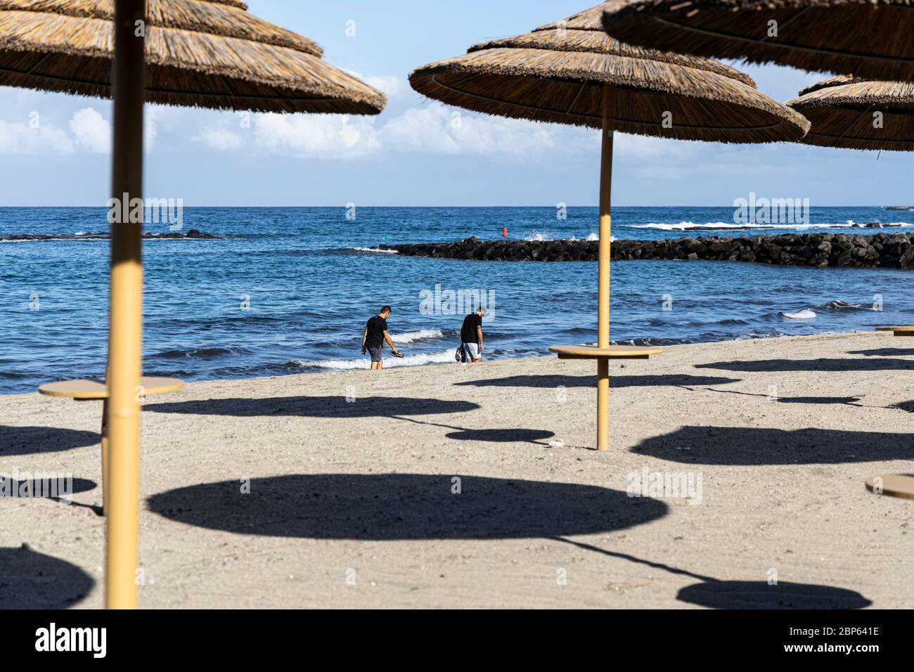 La gente ha intravisto tra gli ombrelloni inutilizzati facendo esercizio a piedi sulla spiaggia di Playa Fanabe durante la fase uno di de-escalation del Covid 1 Foto Stock