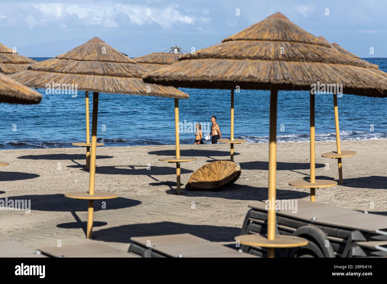 La gente ha intravisto tra gli ombrelloni inutilizzati facendo esercizio a piedi sulla spiaggia di Playa Fanabe durante la fase uno di de-escalation del Covid 1 Foto Stock