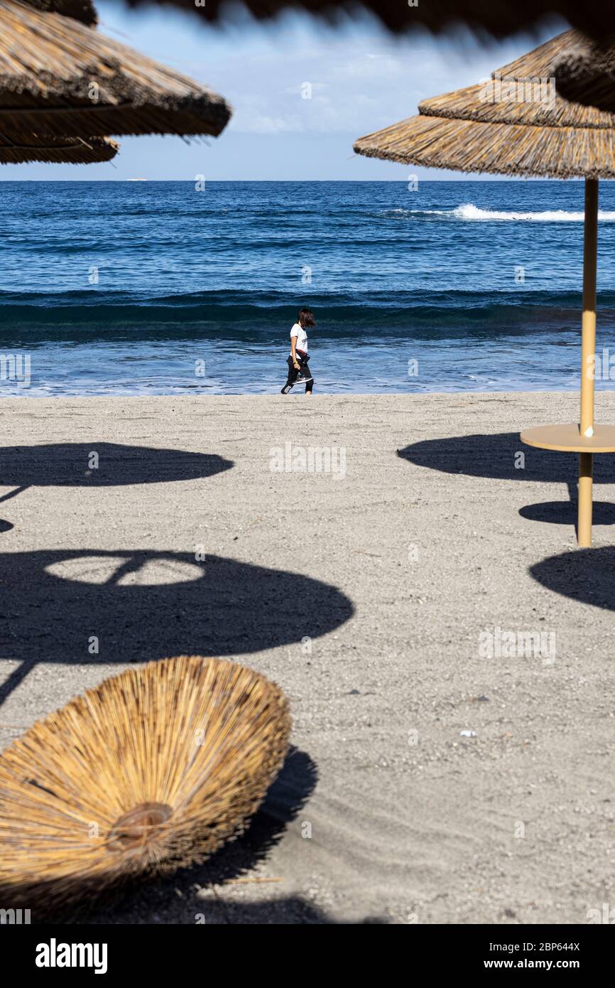 La gente ha intravisto tra gli ombrelloni inutilizzati facendo esercizio a piedi sulla spiaggia di Playa Fanabe durante la fase uno di de-escalation del Covid 1 Foto Stock