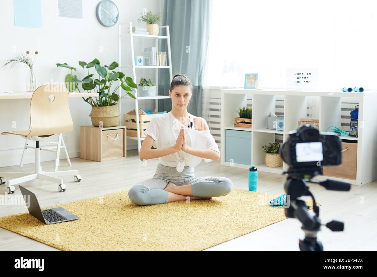 Ritratto a lunghezza intera di giovane donna contemporanea che registra una sessione di yoga online mentre si siede in posizione lotus a casa e si guarda la fotocamera, copia spa Foto Stock