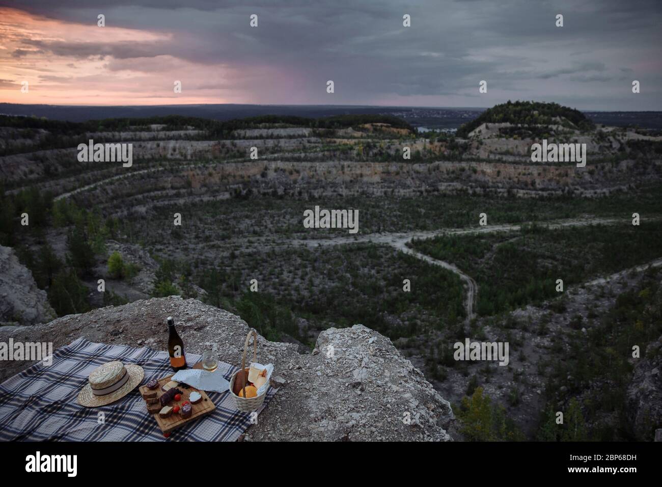 Picnic in una cava abbandonata. Al bordo della pista c'è una coperta, cibo da picnic, un cestino di cibo, bicchieri e vino. Foto Stock