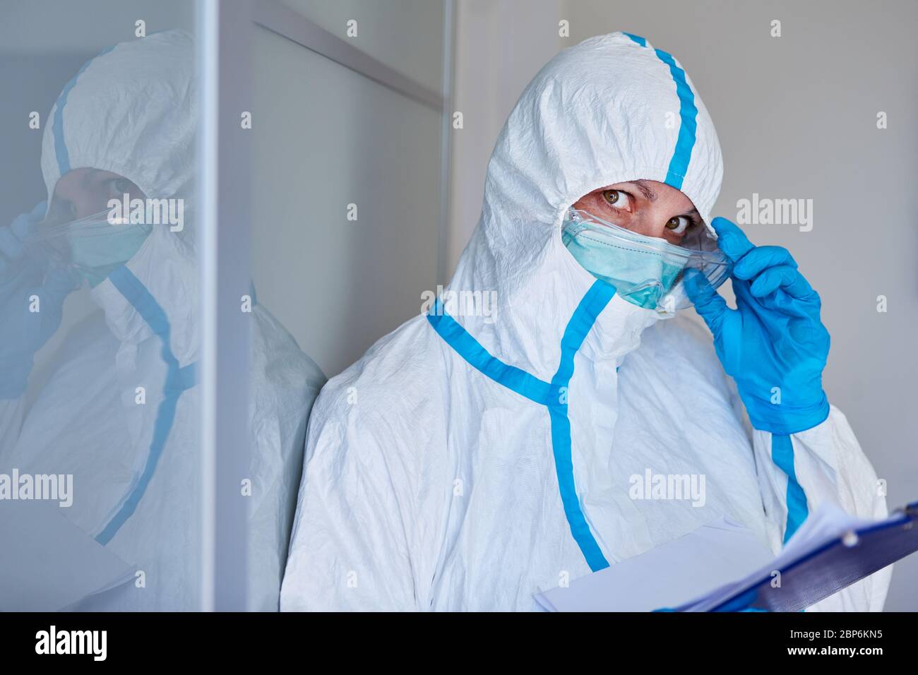 Scout di contenimento o personale infermieristico in abbigliamento protettivo con lista dei visitatori o monitoraggio dei contatti a causa di pandemia di coronavirus Foto Stock