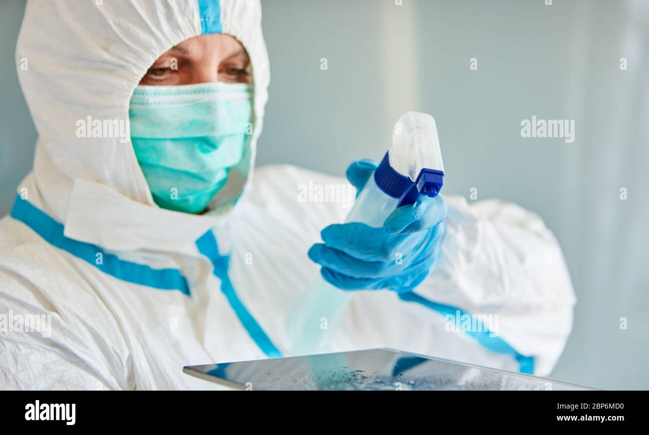 Un detergente in indumenti protettivi disinfetta il touchscreen dal tablet durante la pandemia di coronavirus Foto Stock