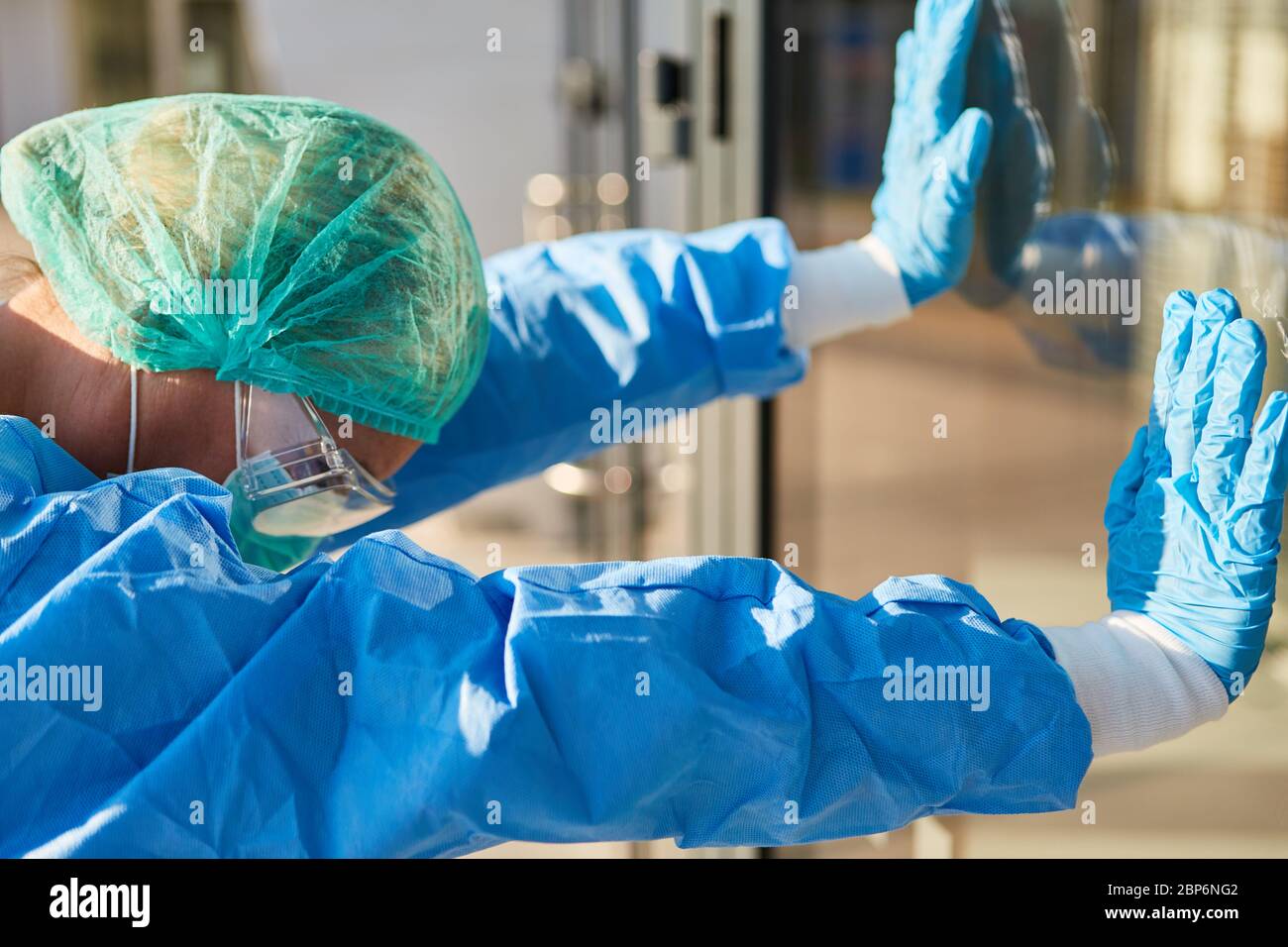 Medico esausto che indossa indumenti protettivi durante la pandemia di coronavirus si appoggia contro la finestra della clinica Foto Stock