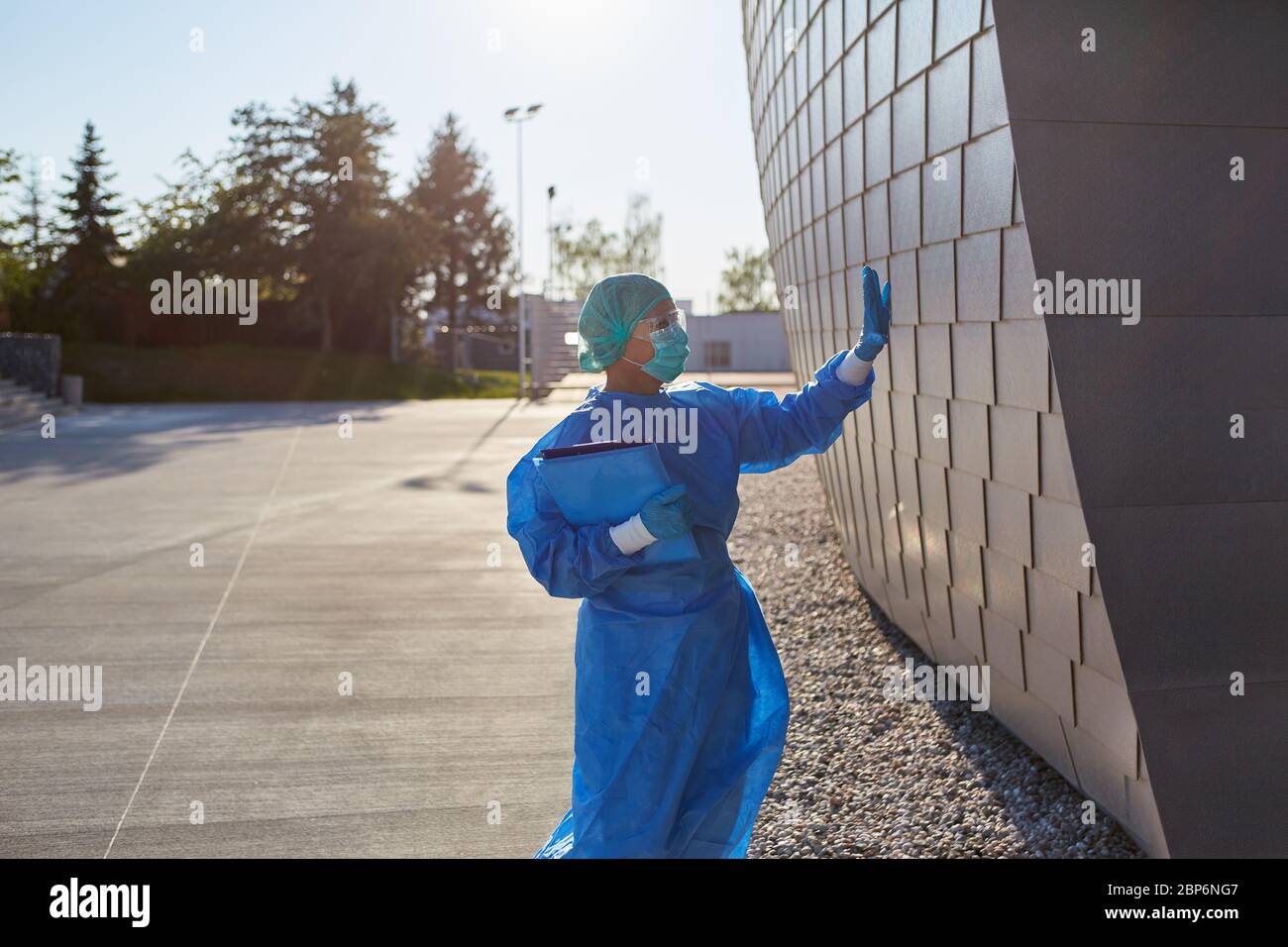 Il chirurgo in abbigliamento protettivo davanti alla clinica fa dei segnali manuali all'ingresso come un gesto durante la pandemia del coronavirus Foto Stock