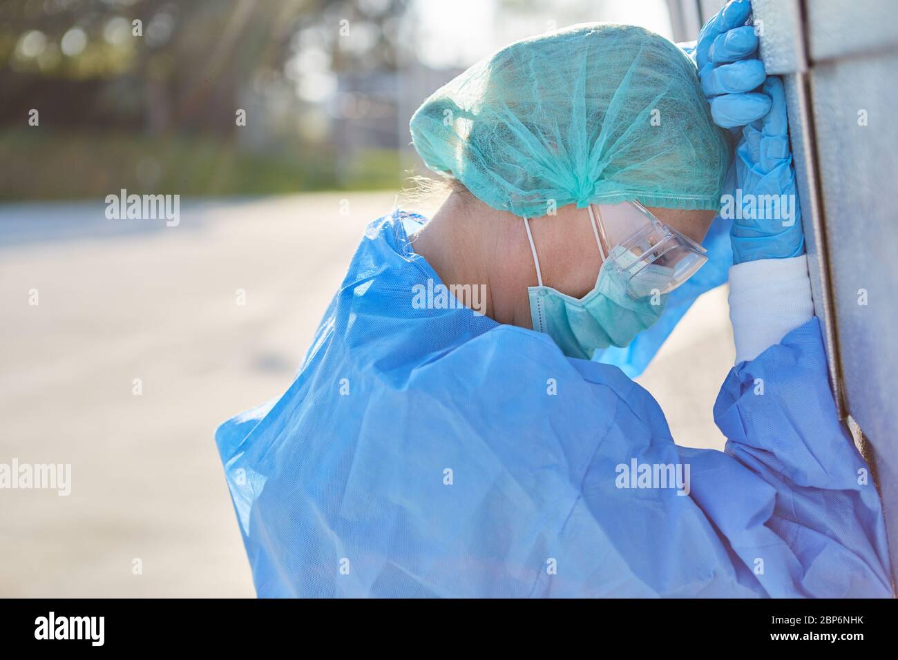 Medico in abbigliamento protettivo durante la pandemia di coronavirus è esaurito e appoggia la testa contro il muro di fronte alla clinica durante la sua pausa Foto Stock