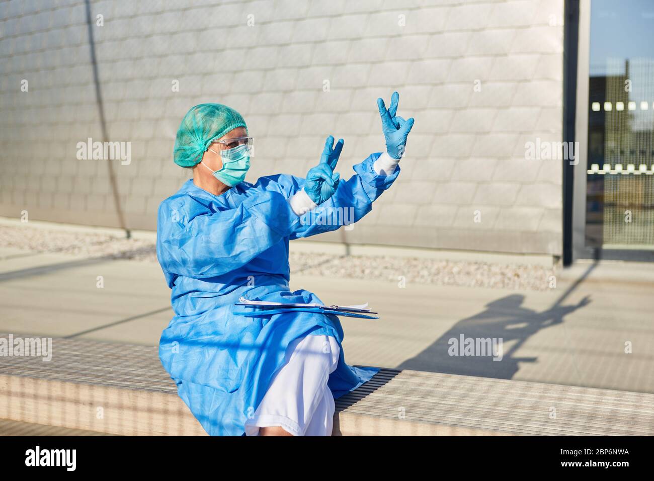 Medico medico o scout di contenimento in abbigliamento protettivo mostra il segno della vittoria come un gesto di vittoria nella lotta contro il coronavirus Foto Stock