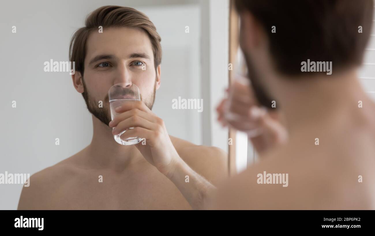 Giovane uomo guardare in bagno specchio acqua potabile Foto Stock