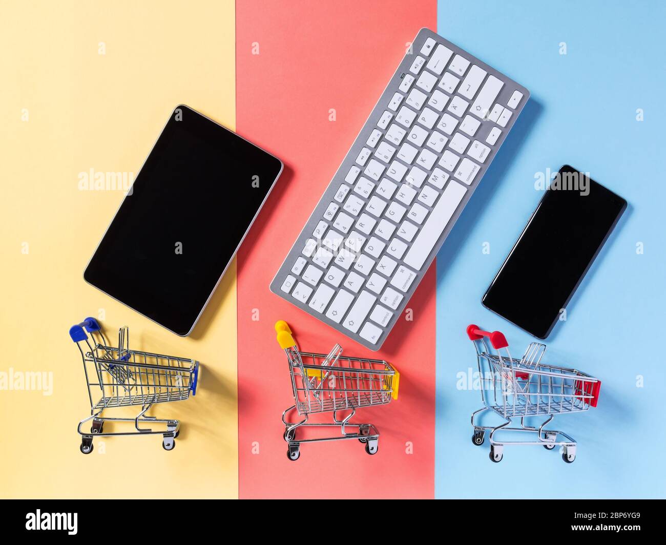 Concetto di shopping online con carrello carrello supermercato, telefono cellulare, tablet e tastiera su sfondo giallo, rosso e blu colorato. E-comme Foto Stock