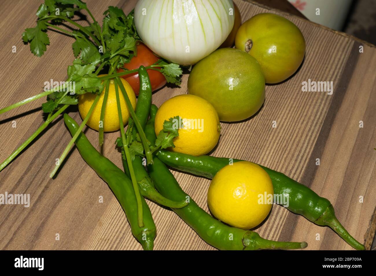 Verdure di vario genere su tavola di legno, cipolla, pomodori, limone, peperoncino verde e coriandolo. Foto Stock