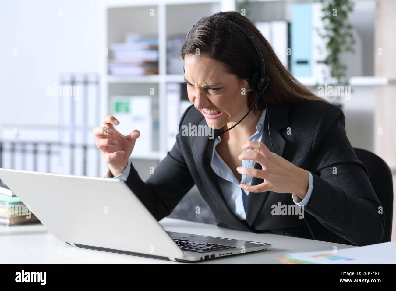 Donna di telemarketer arrabbiata che guarda il computer portatile seduto su una scrivania in ufficio Foto Stock