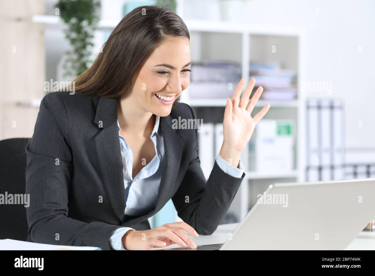 Felice donna dirigente saluto su videocall su computer portatile seduto sulla sua scrivania in ufficio Foto Stock