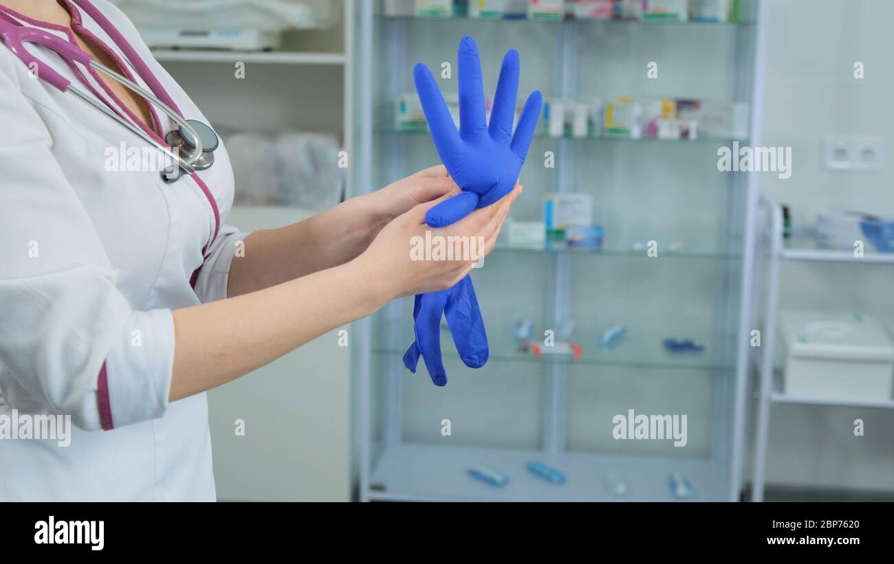 Giovani donne medico caucasico in camice medico bianco e stetoscopio viola gonfia un guanto di gomma blu. Controlla se è presente una perdita e può essere utilizzata. Foto Stock