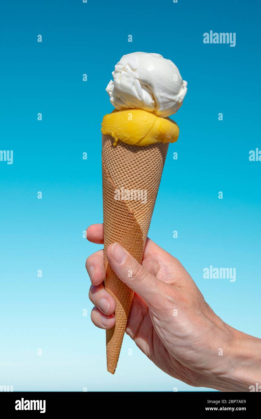 Mano tenendo un cono di icecream su sfondo blu cielo Foto Stock