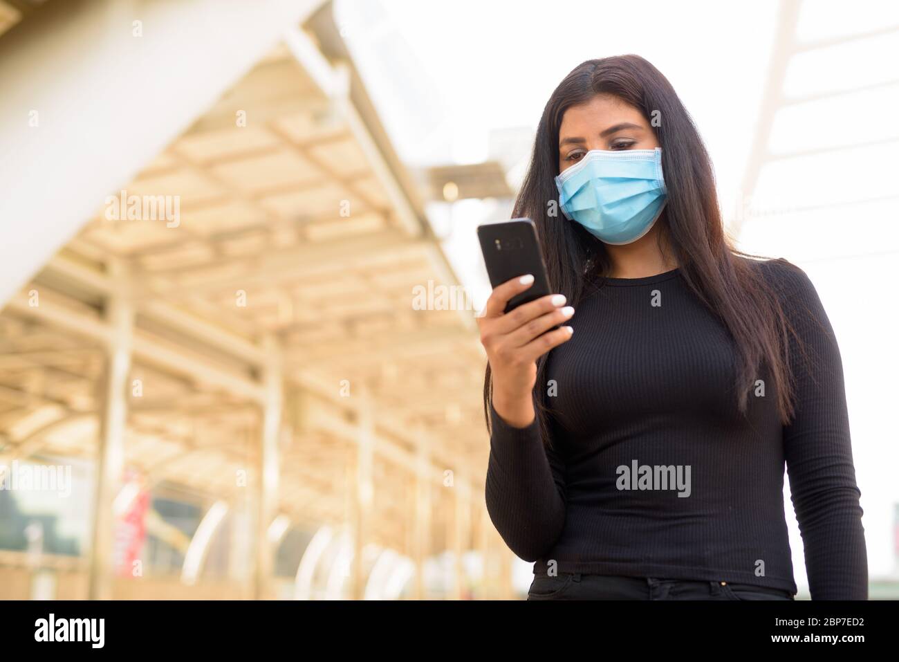 Giovane donna indiana con maschera per la protezione da focolaio di virus corona utilizzando il telefono al ponte Skywalk Foto Stock