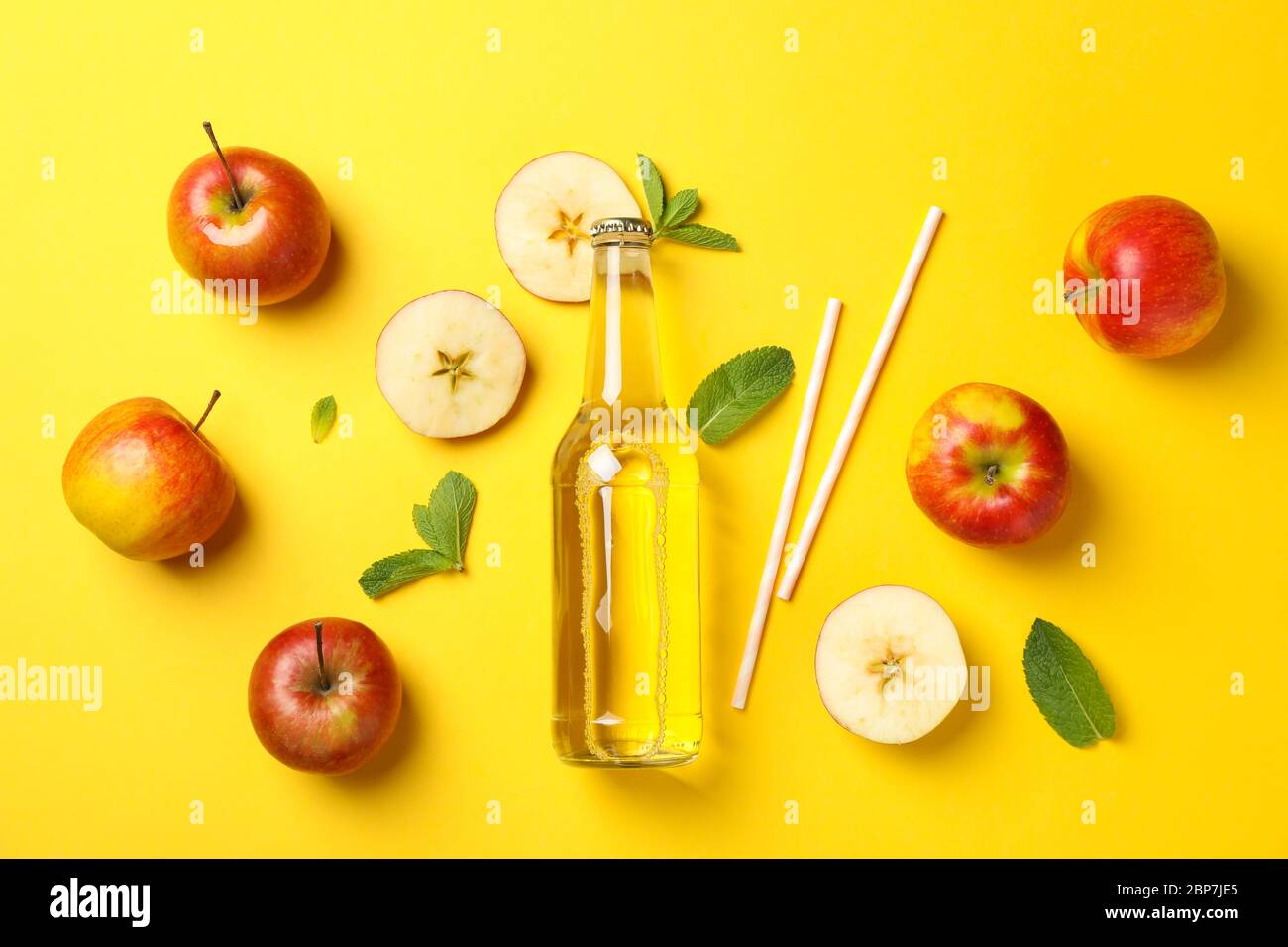 Composizione con sidro, mele e cannucce su fondo giallo Foto Stock