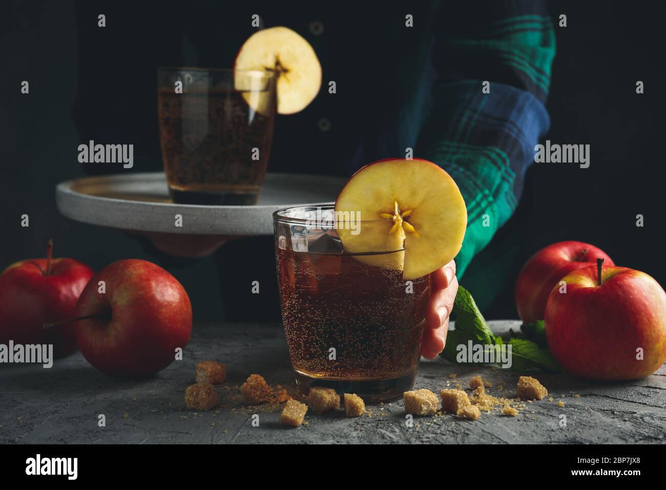 Femmina con vassoio per vetro di sidro. Composizione con sidro e mela su tavola grigia Foto Stock