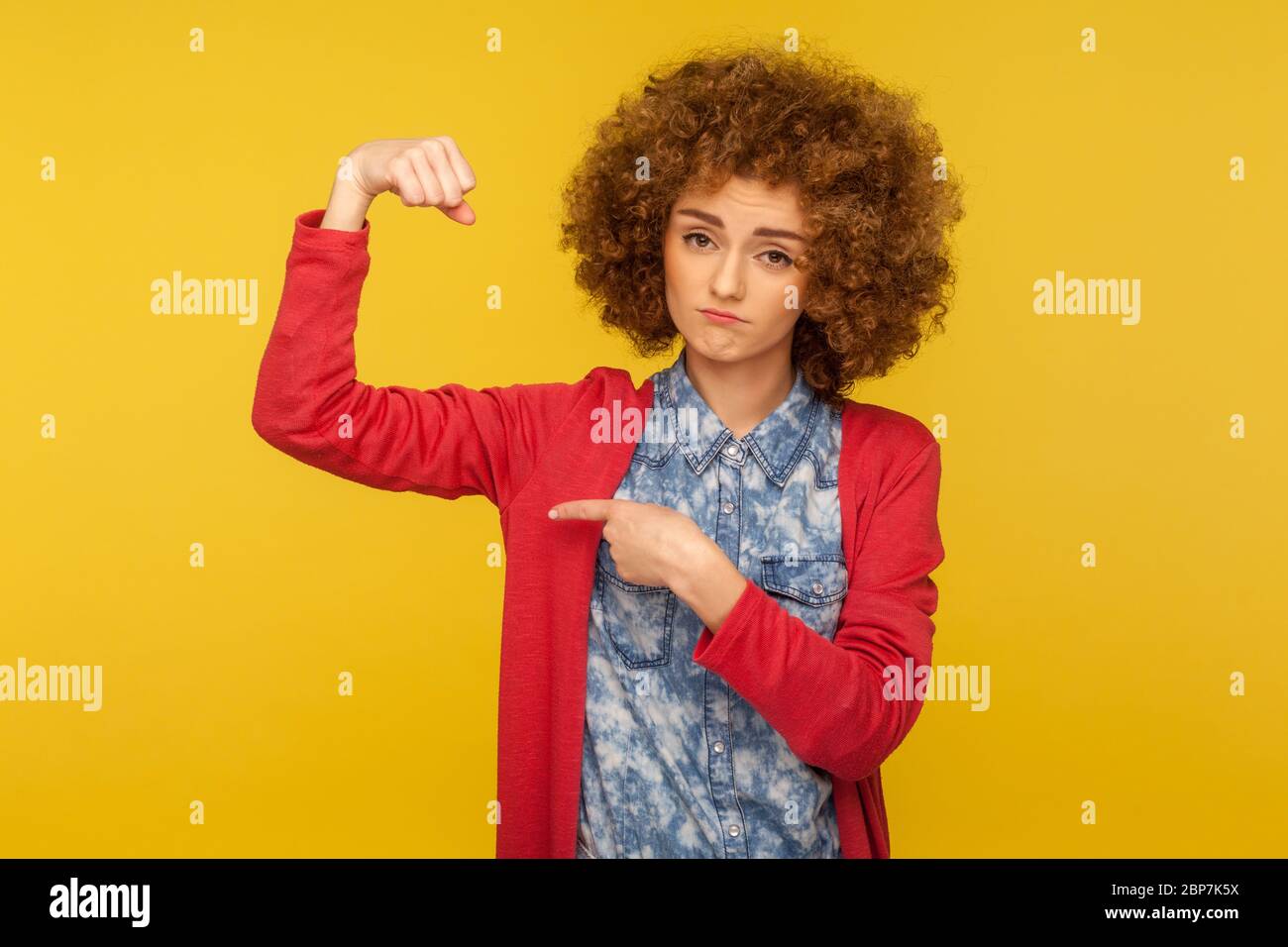 Guarda, sono forte! Ritratto di donna sicura con capelli ricci che alzano il braccio puntando bicipiti come metafora del potere e dell'indipendenza, concetto di diritti femminili Foto Stock