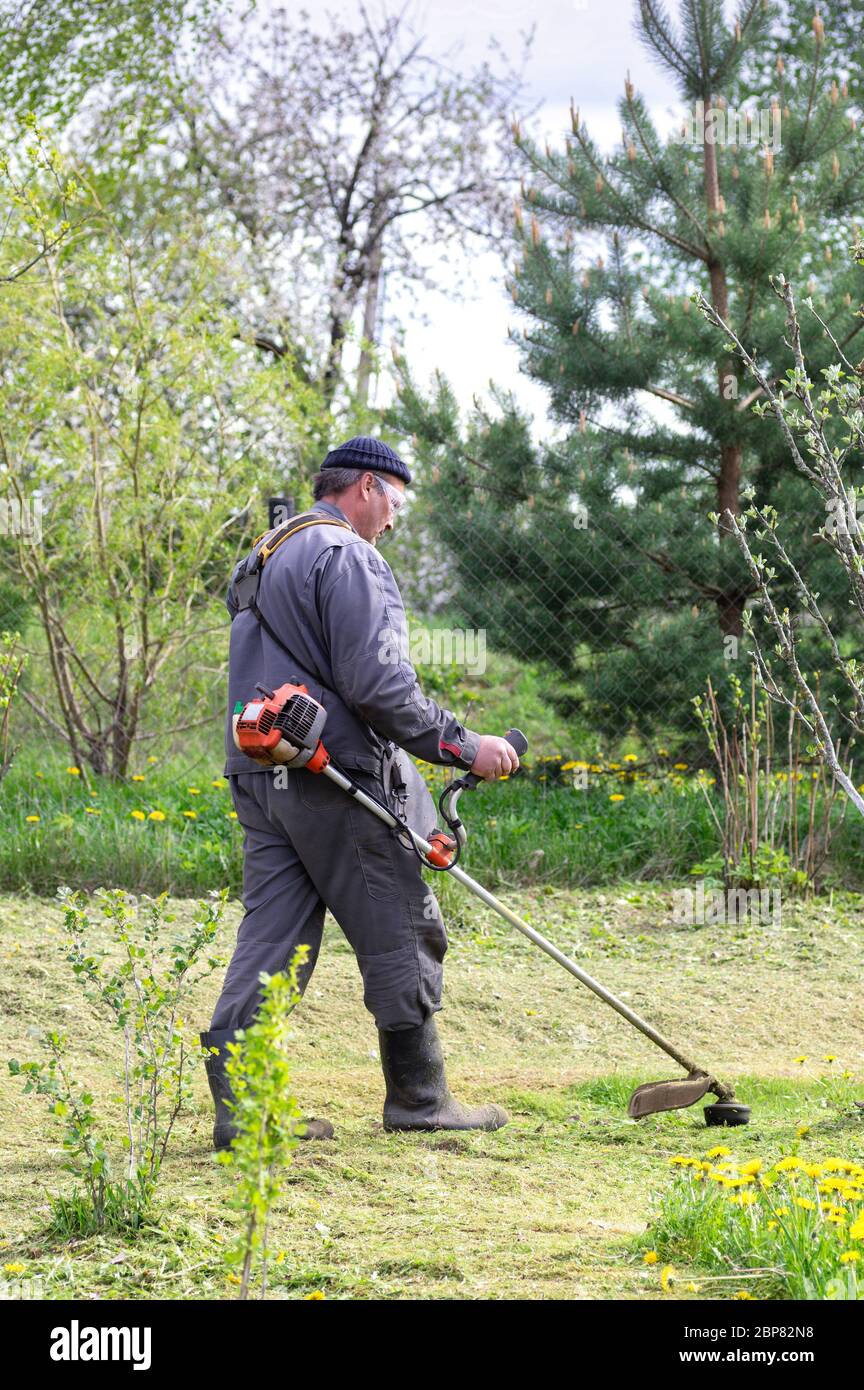 Coltivatore falcia erba nel giardino di primavera. Il concetto di cura per un complotto personale. Utilizzare un rifinitore da giardino. Foto Stock