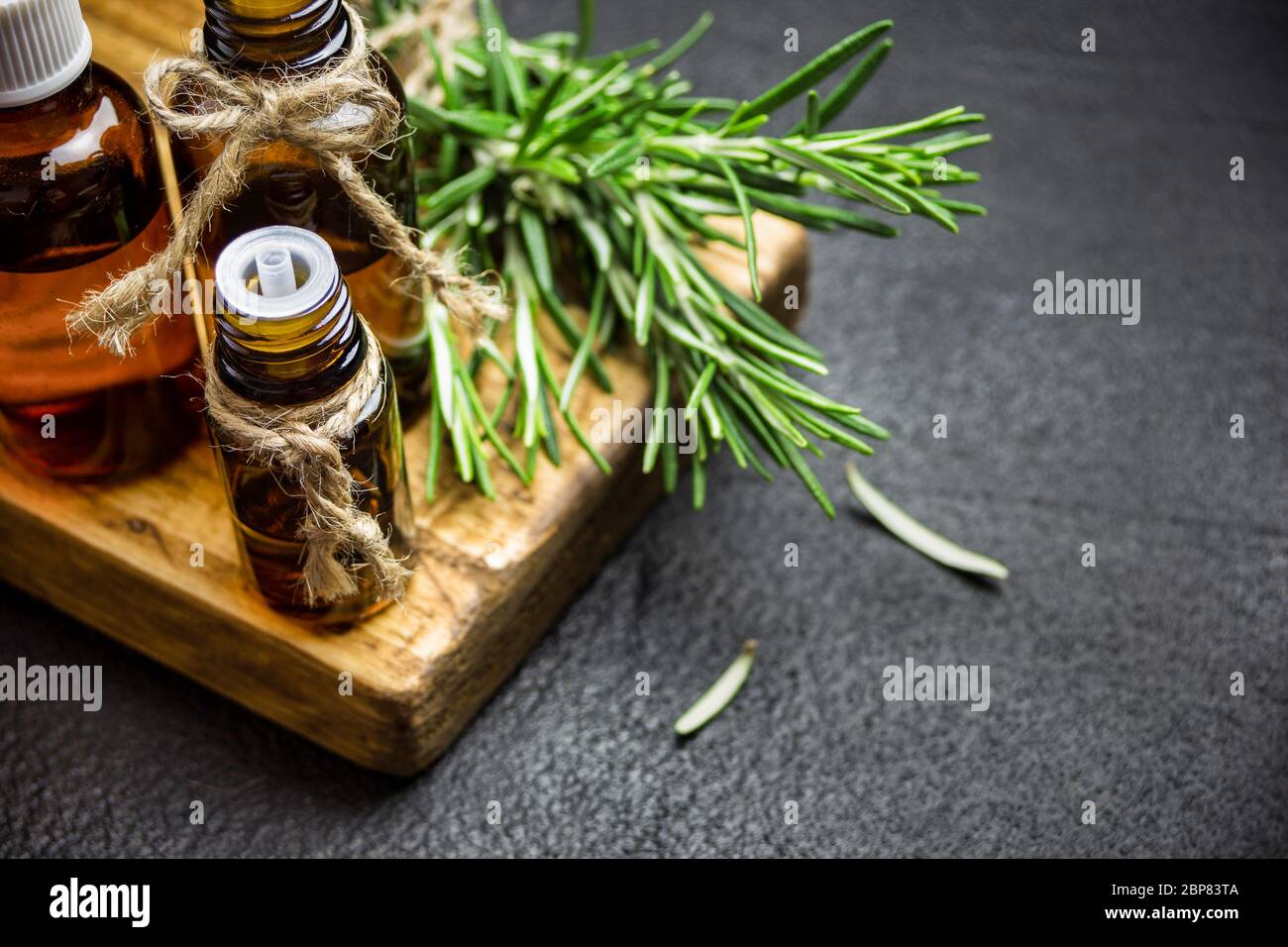 Rami di erbe di rosmarino e bottiglie di olio essenziale di rosmarino su fondo di pietra nera. Concetto di aromaterapia erboristica. Foto Stock