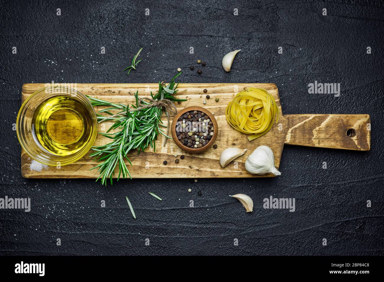Ingredienti per la cucina italiana, pasta, erbe, spezie e olio d'oliva su tavola di pietra nera. Vista dall'alto con spazio per la copia. Foto Stock